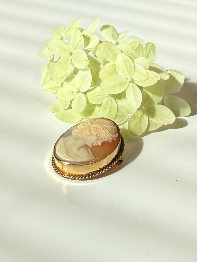 Angled view of vintage carved shell cameo showing textured gold-filled border