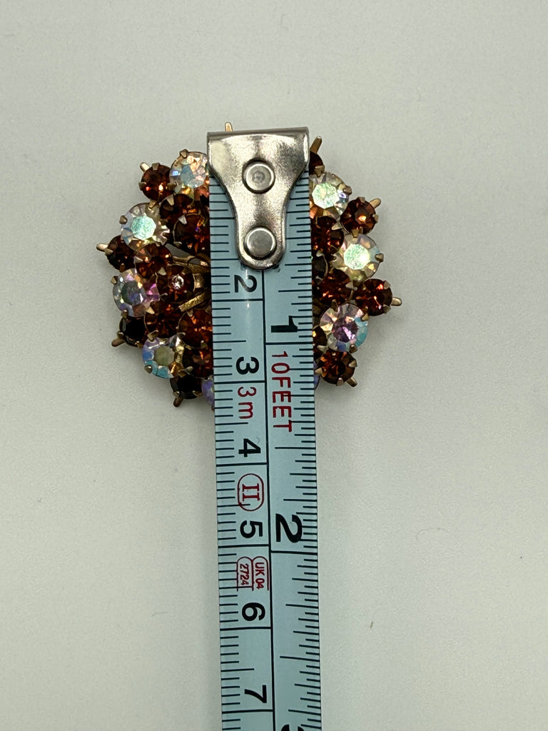 Vintage Aurora Borealis starburst brooch beside measuring tape showing approximately 1.5 inch width