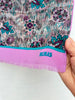 Close-up of a vintage Bill Blass silk scarf featuring a colourful floral print, pink border and fashionable fringed ends.