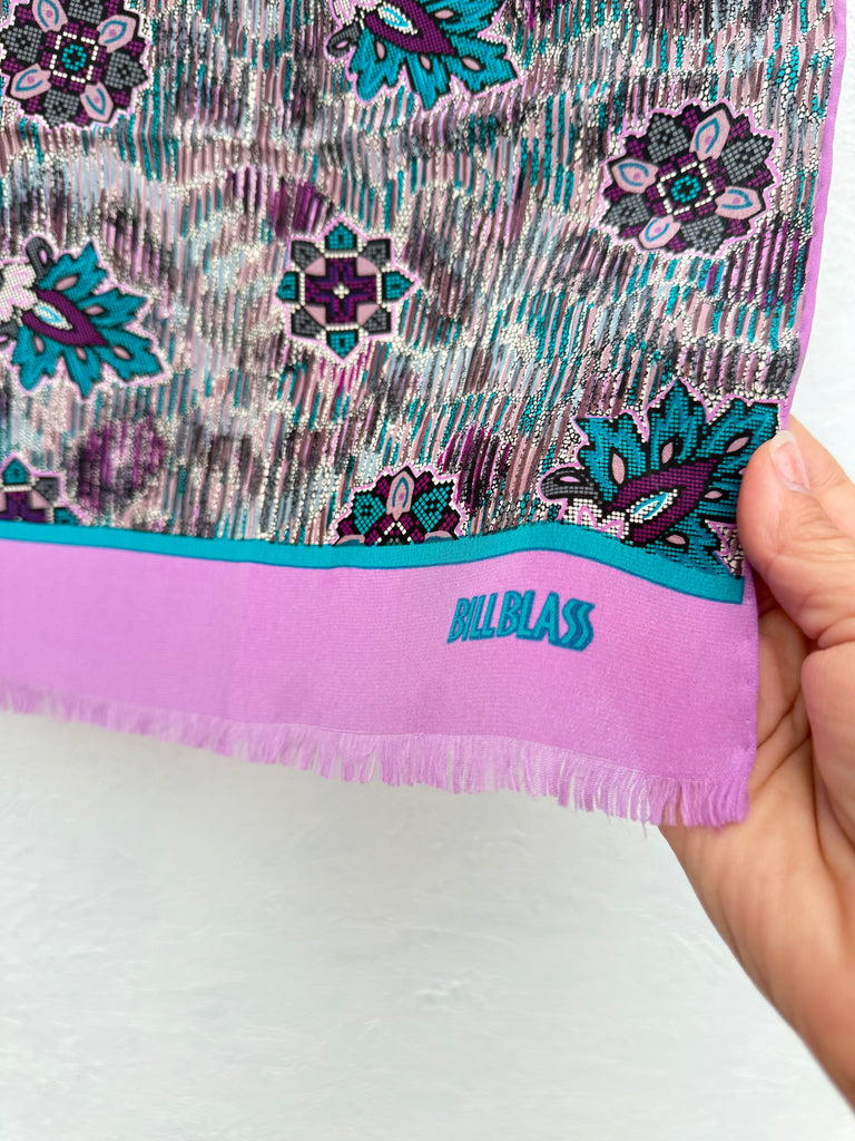 Close-up of a vintage Bill Blass silk scarf featuring a colourful floral print, pink border and fashionable fringed ends.