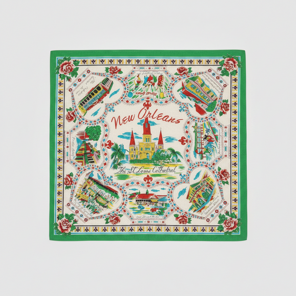 A square New Orleans-themed scarf laid flat on a textured concrete surface. The scarf features a white background with a vibrant green border, red roses, and multiple colorful illustrations of New Orleans landmarks including the Cathedral of Saint Louis, the Mississippi Riverboat, and the French Quarter, with 'New Orleans' written in red script in the center.