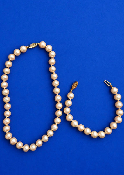 Vintage cream faux pearl necklace and matching bracelet set displayed on a blue background