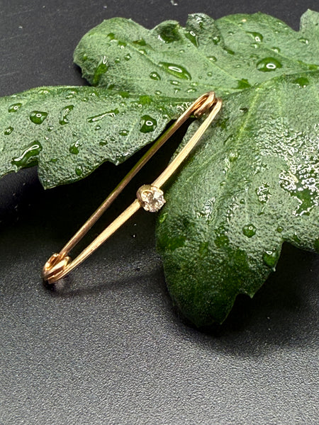 Antique 14K yellow gold safety pin brooch with Old Mine Cut diamond displayed on green leaf