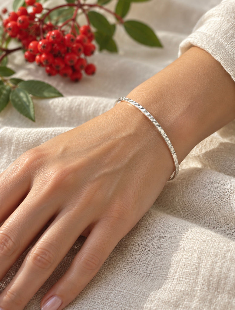 Slim hammered sterling silver bangle bracelet worn on wrist