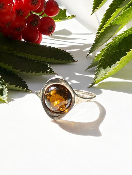 Vintage Baltic cognac amber sterling silver ring displayed among greenery and red berries