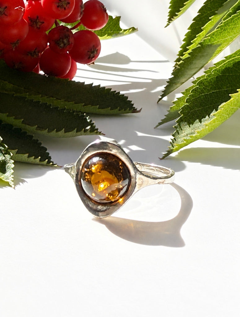 Vintage Baltic cognac amber sterling silver ring displayed among greenery and red berries