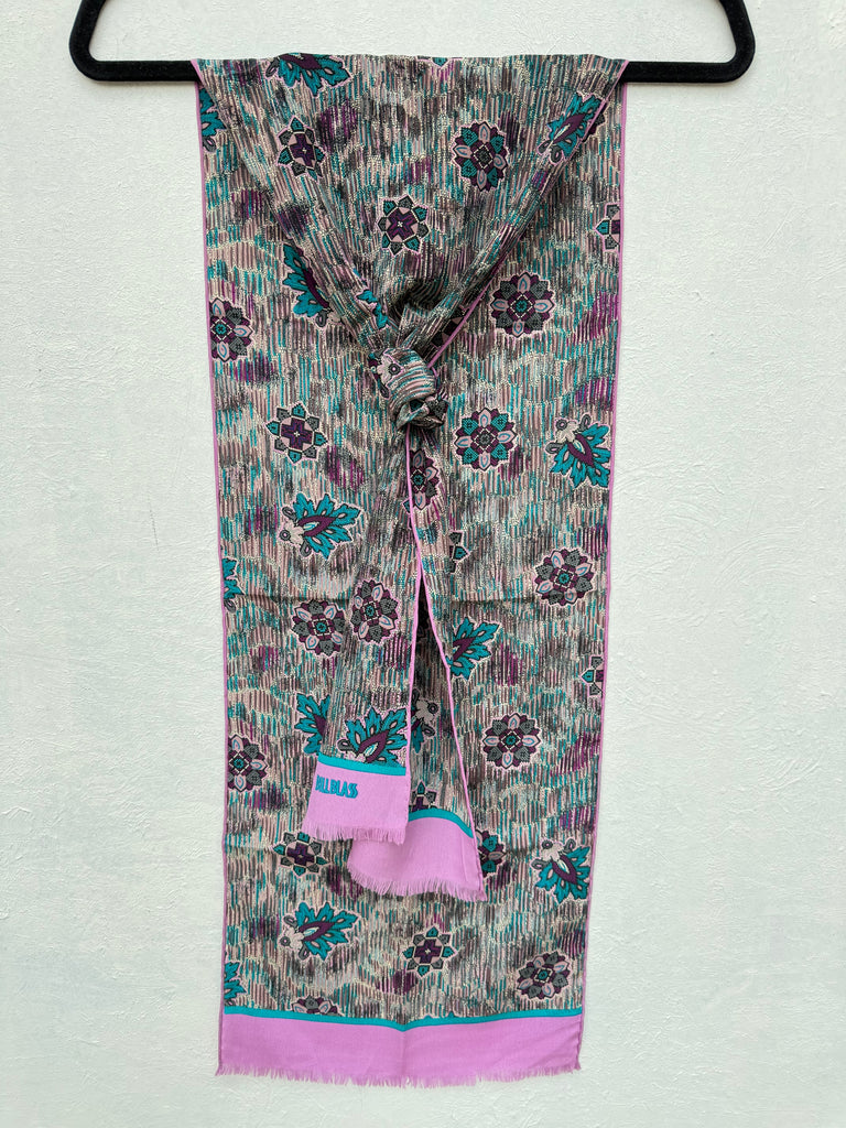A patterned scarf with a tie knot, featuring a grey, purple, and teal floral design with a bright pink border and tassel.