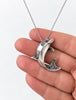 Sterling silver dolphin pendant held in hand showing scale and detail