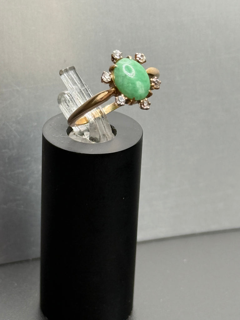 Vintage 14K gold green jade cabochon ring with round diamond halo displayed on black stand