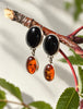 Vintage amber and black onyx sterling silver drop earrings displayed with botanical leaves