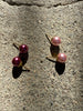 Pair of raspberry pink faux pearl stud earrings displayed on textured grey background