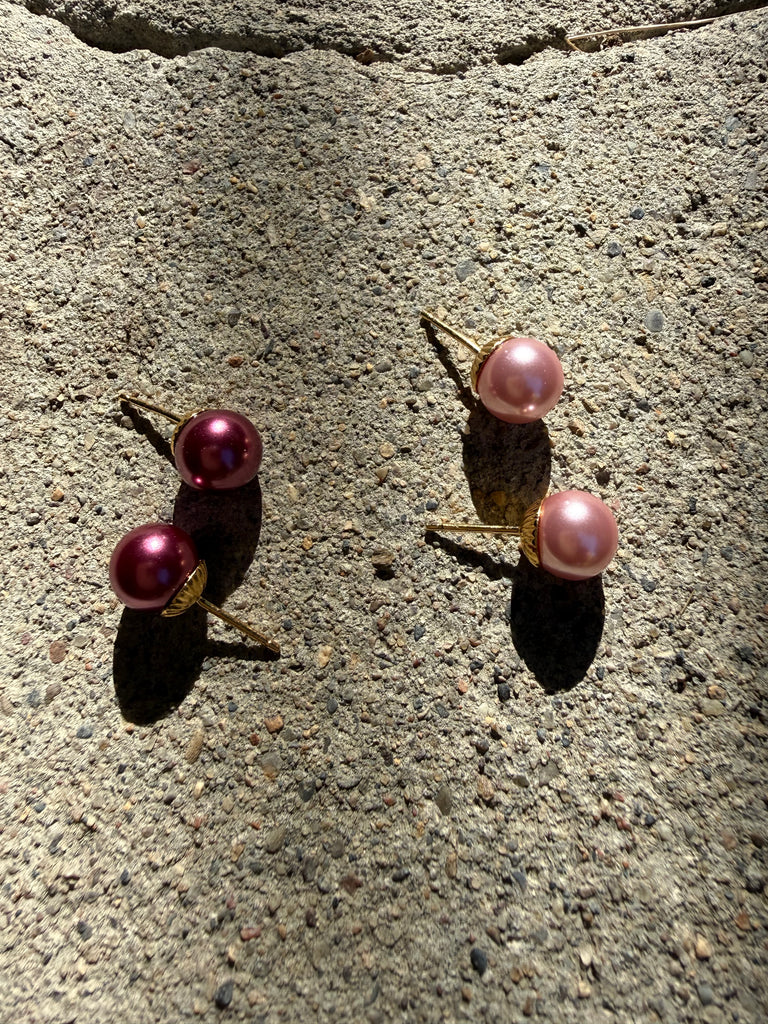 Pair of raspberry pink faux pearl stud earrings displayed on textured grey background