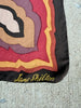 A close-up of a vintage Jane Shilton scarf laid flat. The scarf features a retro concentric floral pattern in shades of red, yellow, purple, beige, and black, with 'Jane Shilton' embroidered in gold script at the bottom corner.