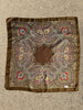 A square silk scarf with an intricate paisley pattern, laid flat. The design features a central brown medallion surrounded by detailed paisley motifs in red, gold, blue, and green, all framed by a solid brown border.
