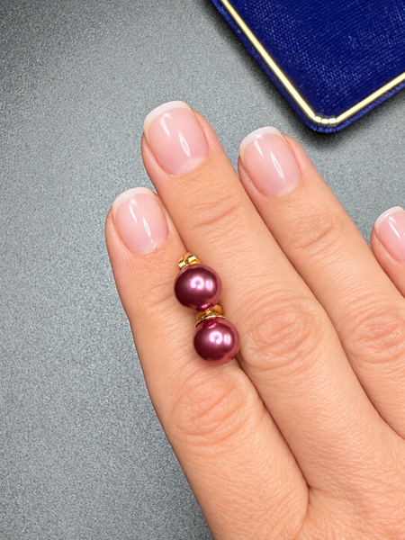 Vintage dark pink faux pearl stud earrings with gold-tone settings worn on hand