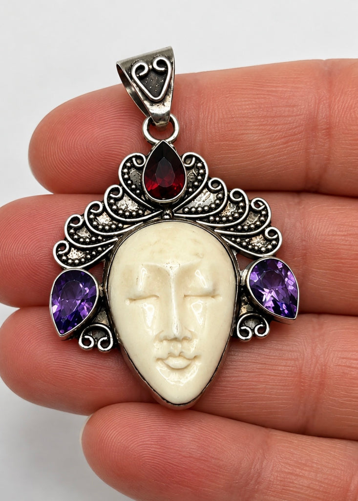 Balinese sterling silver goddess pendant shown in hand with carved face, purple amethysts and red garnet