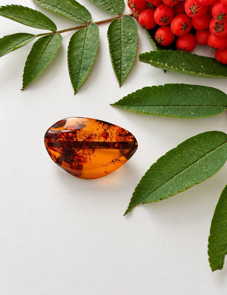 Vintage Baltic amber brooch with polished freeform cognac amber photographed among green leaves and red berries