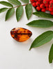 Vintage Baltic amber brooch with polished freeform cognac amber photographed among green leaves and red berries