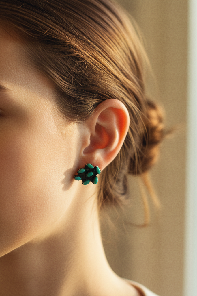 A pair of small cluster stud earrings with oval turquoise-blue stones set in dark metal, placed on a dark textured surface.