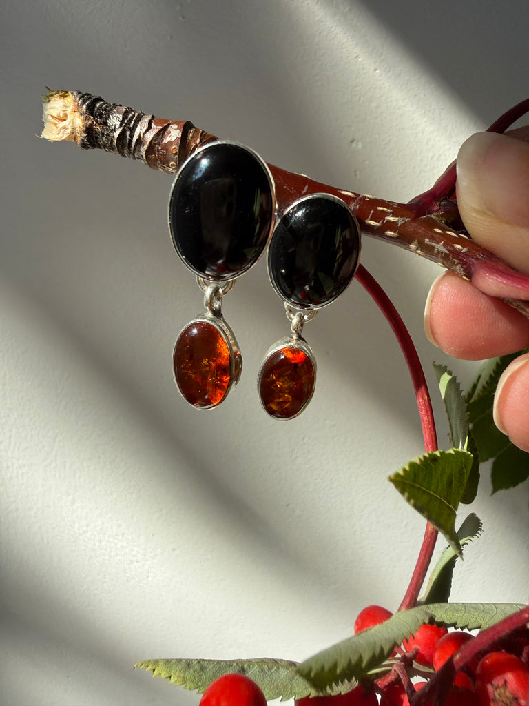 Vintage natural amber and black onyx silver dangle earrings hanging beside red berries