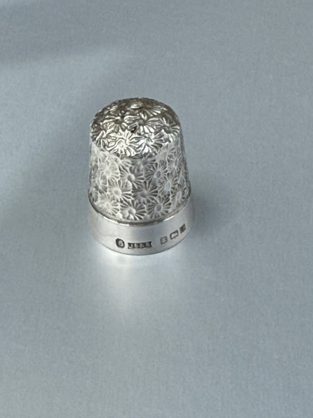 Silver thimble with floral pattern on a gray background