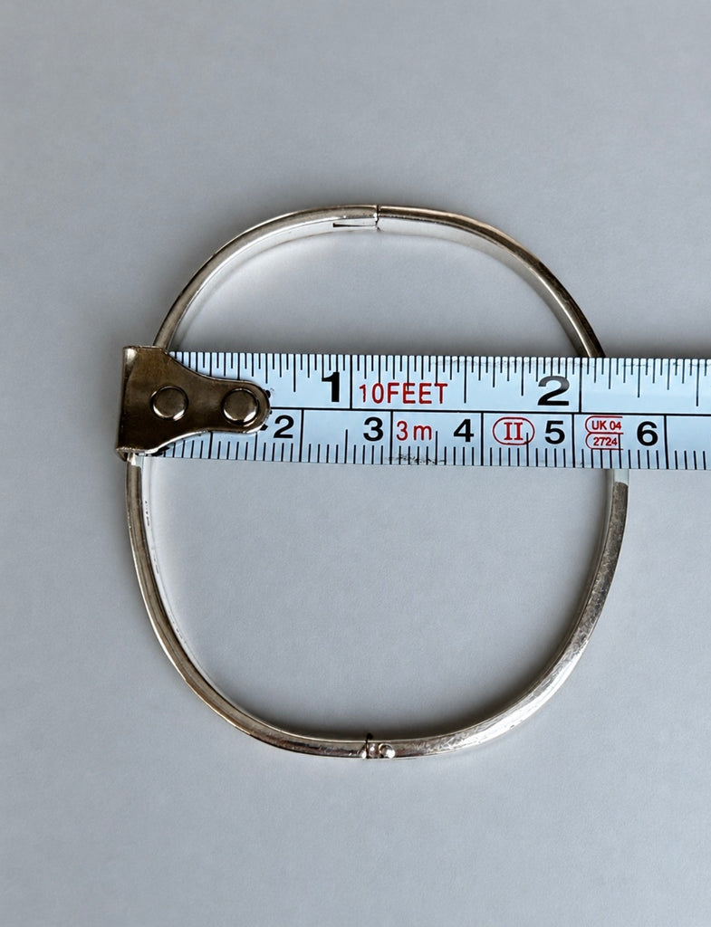 Vintage sterling silver hinged bangle beside measuring tape showing width