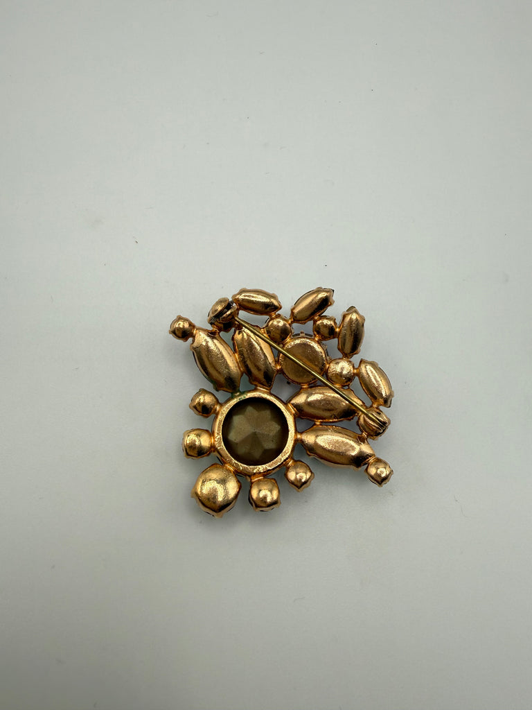 Back of unsigned vintage rhinestone brooch showing gold tone metal setting and pin-back closure