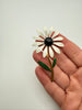 White enamel daisy brooch with dark green leaves and slender gold tone stem shown in hand for scale