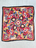 A square silk scarf featuring a vibrant, multicolored abstract paisley pattern with a solid black border, laid flat.