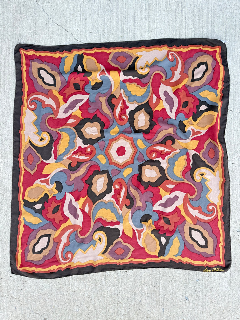 A square silk scarf featuring a vibrant, multicolored abstract paisley pattern with a solid black border, laid flat.