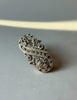 An ornate silver-toned paisley brooch embellished with small dark stones, resting on a plain gray surface. Sterling Silver 