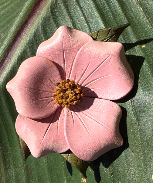 Vintage Alberta Wild Rose pink leather flower brooch with green leaves displayed on a large green leaf