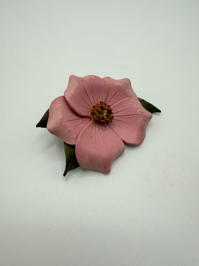 Angled view of handmade pink leather Wild Rose brooch showing dimensional petals and floral centre