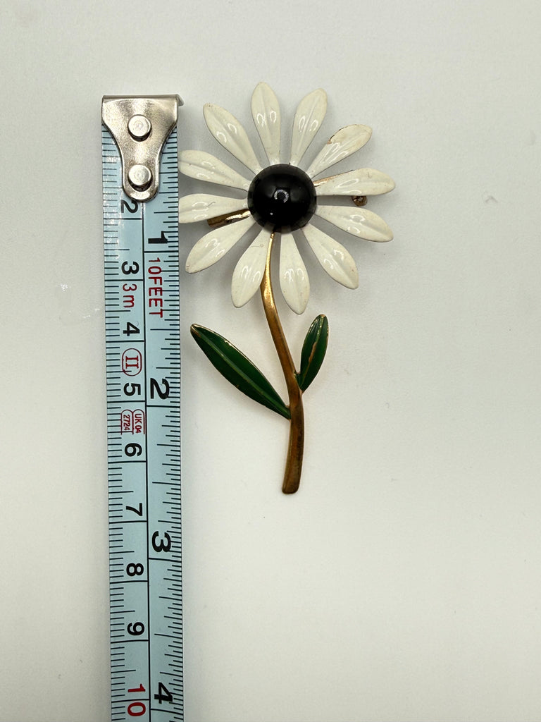 Vintage white enamel daisy brooch beside measuring tape showing approximately 2.5 inch length