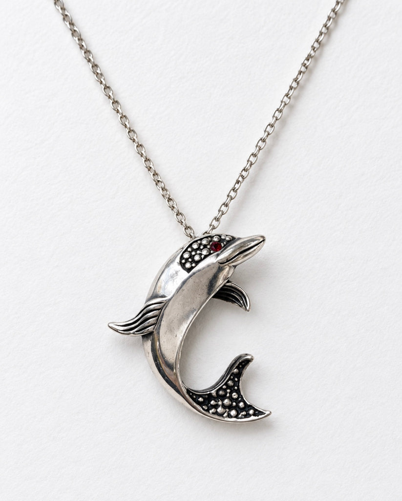 Close-up of sculptural sterling silver dolphin pendant with tiny red eye