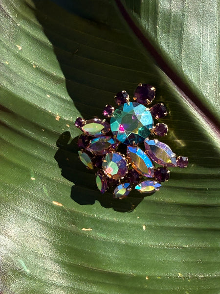 Vintage aurora borealis rhinestone brooch with iridescent multicolour stones and purple accents in a gold tone setting on green leaf
