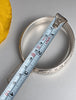 Vintage sterling silver hinged bangle beside measuring tape showing width and size