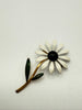 Vintage white green and black enamel daisy flower brooch with long gold tone stem on light background