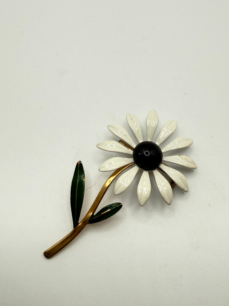 Vintage white green and black enamel daisy flower brooch with long gold tone stem on light background