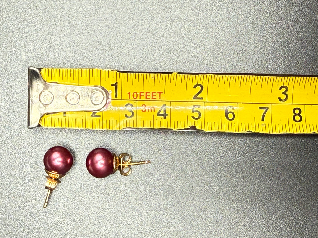 Dark pink faux pearl stud earrings beside measuring tape showing approximately 10 mm diameter