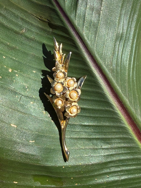 Vintage Marcel Boucher gladiolus brooch with sculptural gold plated leaves and faux pearl flower accents displayed on green leaf