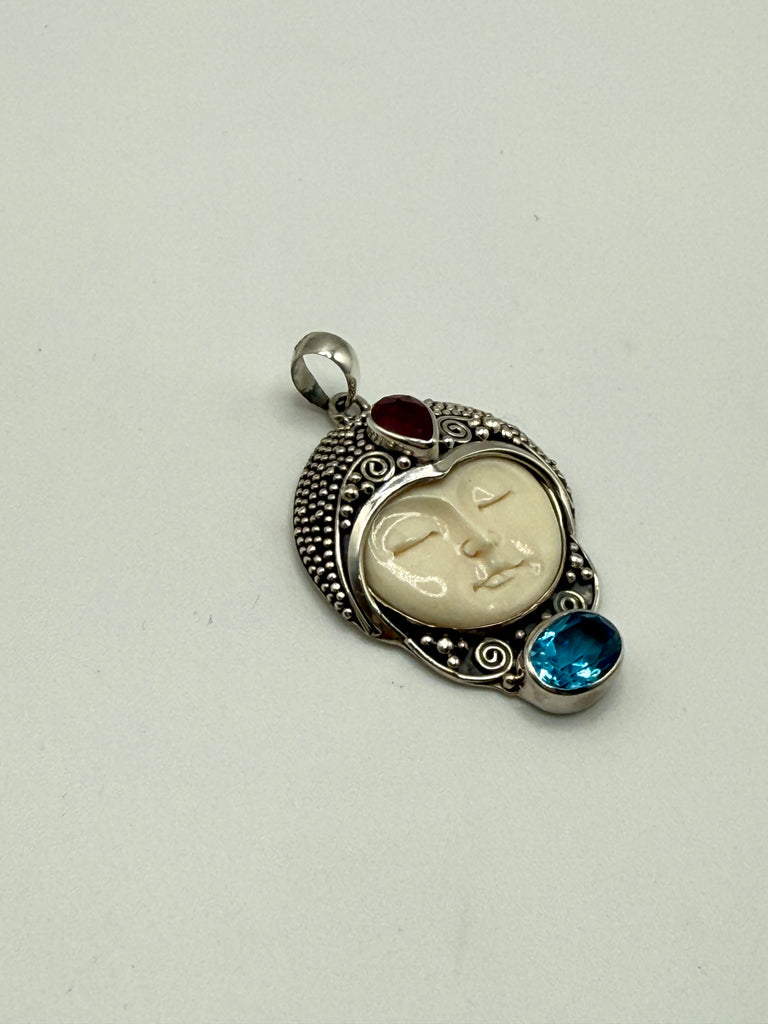 Angled view of vintage Balinese silver pendant with carved cream portrait and colourful stone accents