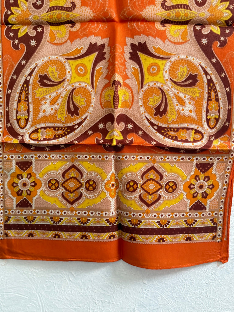 Close-up of ornate paisley floral border on vintage orange silk scarf. 