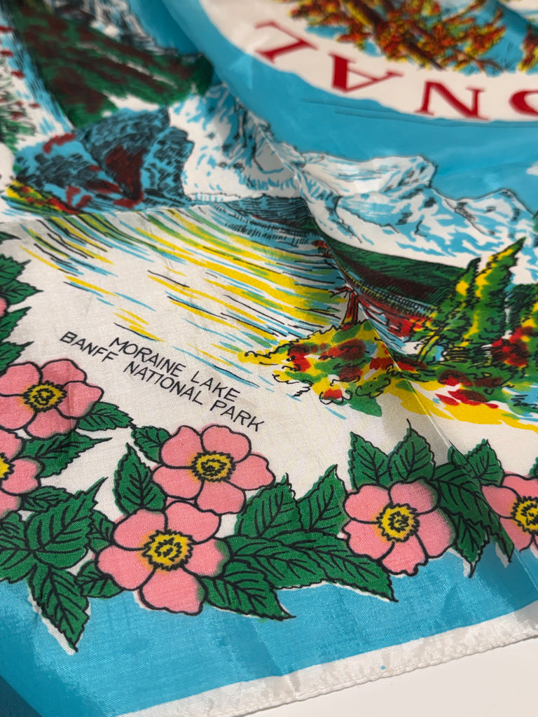 Close-up of vintage Banff National Park scarf with illustrated Canadian Rockies landmarks and pink flowers. 