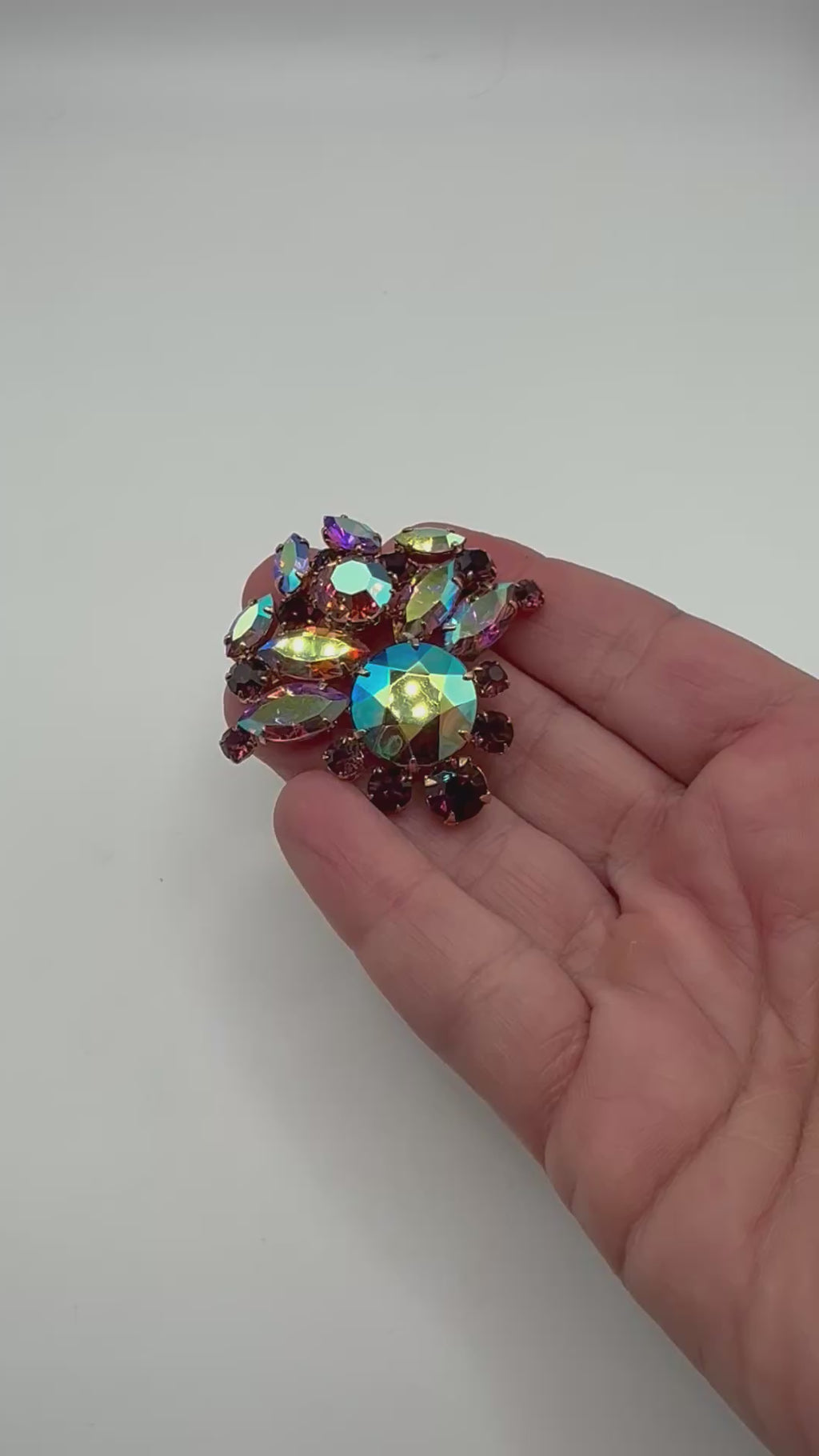 Vintage aurora borealis and purple rhinestone statement brooch shown in hand for scale