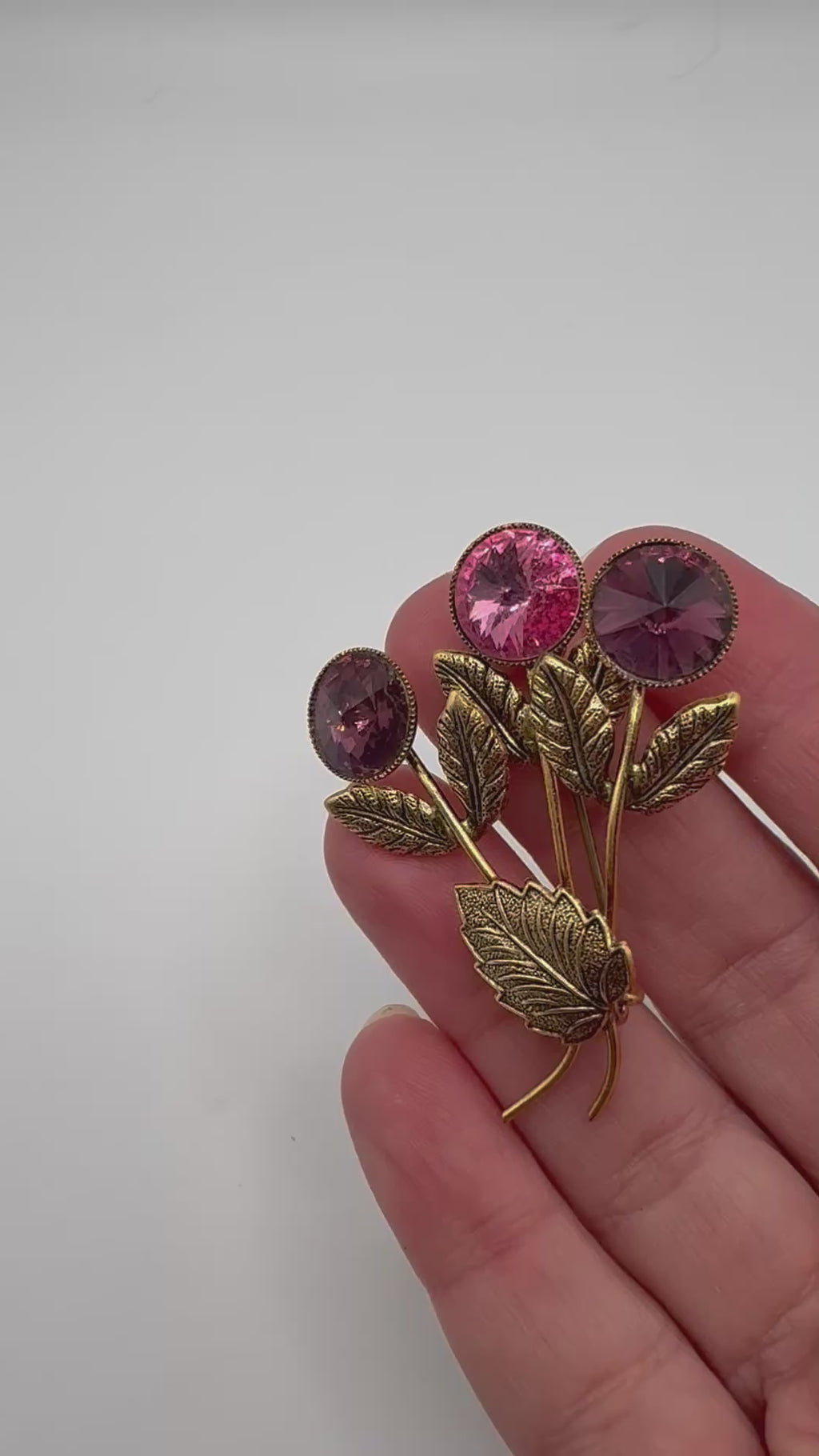 Vintage Made in Austria crystal brooch shown in hand with three pink and purple stones