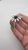 Vintage enamel daisy flower brooch shown in hand with white petals black centre and green leaves